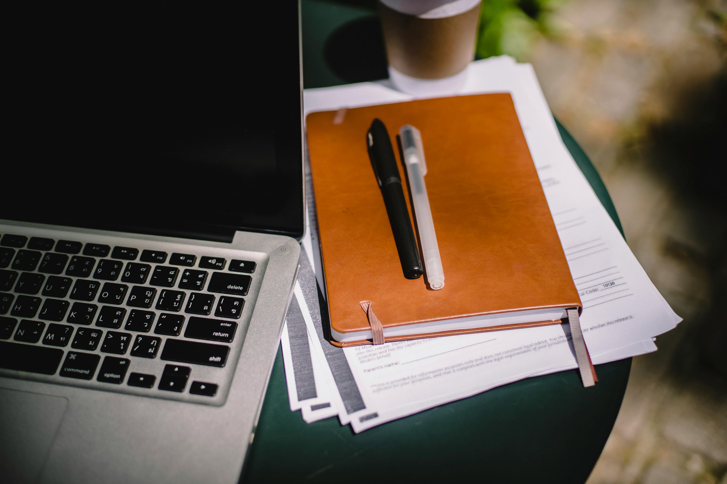 A notebook and pens next to a computer.